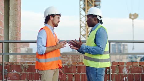 multiethnic two men in hardhats at the constructing site. african american and caucasian builder and architect talking, solving some problems and shaking hands.