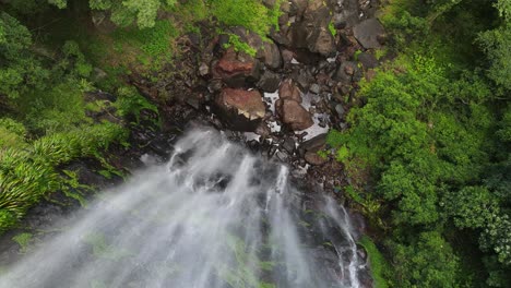 Spectacular-view-looking-down-on-a-misty-rainforest-waterfall-cascading-into-a-lush-green-natural-swimming-pool