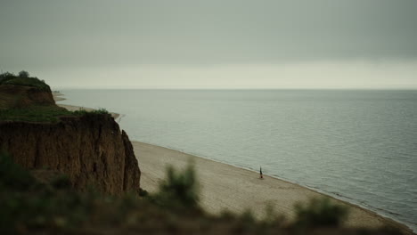 scenic green hill rising over sandy beach cloudy day. gray skyline over calm sea