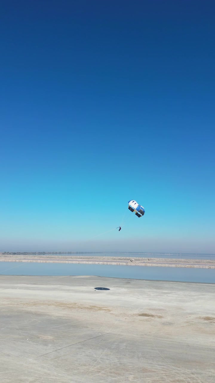A cinematic aerial shot of a paraglider soaring above the vast, minimalist landscape of the Sambhar salt lake. Ideal for travel documentaries and adventure sports content.