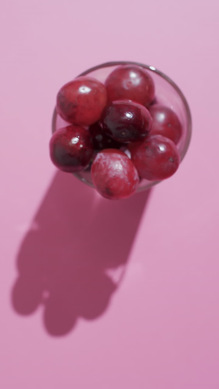 Vertical video of red grapes in glass with copy space on pink background