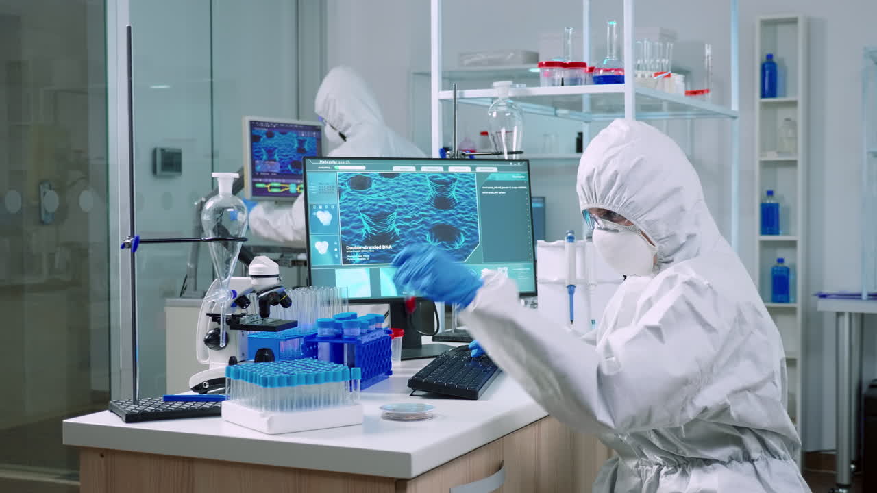 カバーオールを着た化学者血液サンプルをチェックしコンピューターでメモを取っています