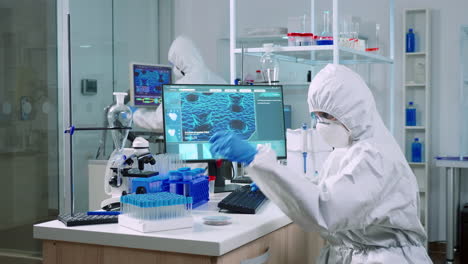 Chemist-in-coverall-checking-blood-samples-taking-notes-on-computer