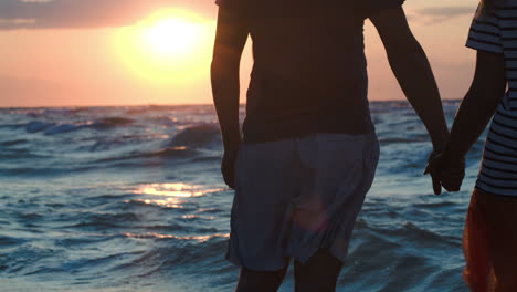 loving couple holding hands by rough wavy sea at sunset