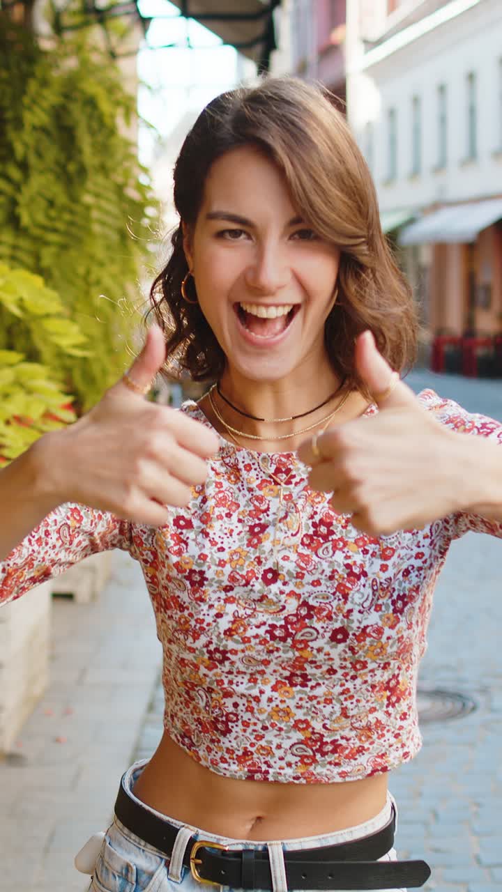 Mulher jovem mostrando polegares para cima como sinal positivo algo bom feedback positivo na rua da cidade