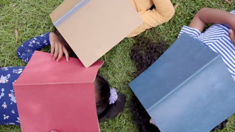 in school, three biracial girls are lying on grass, reading books