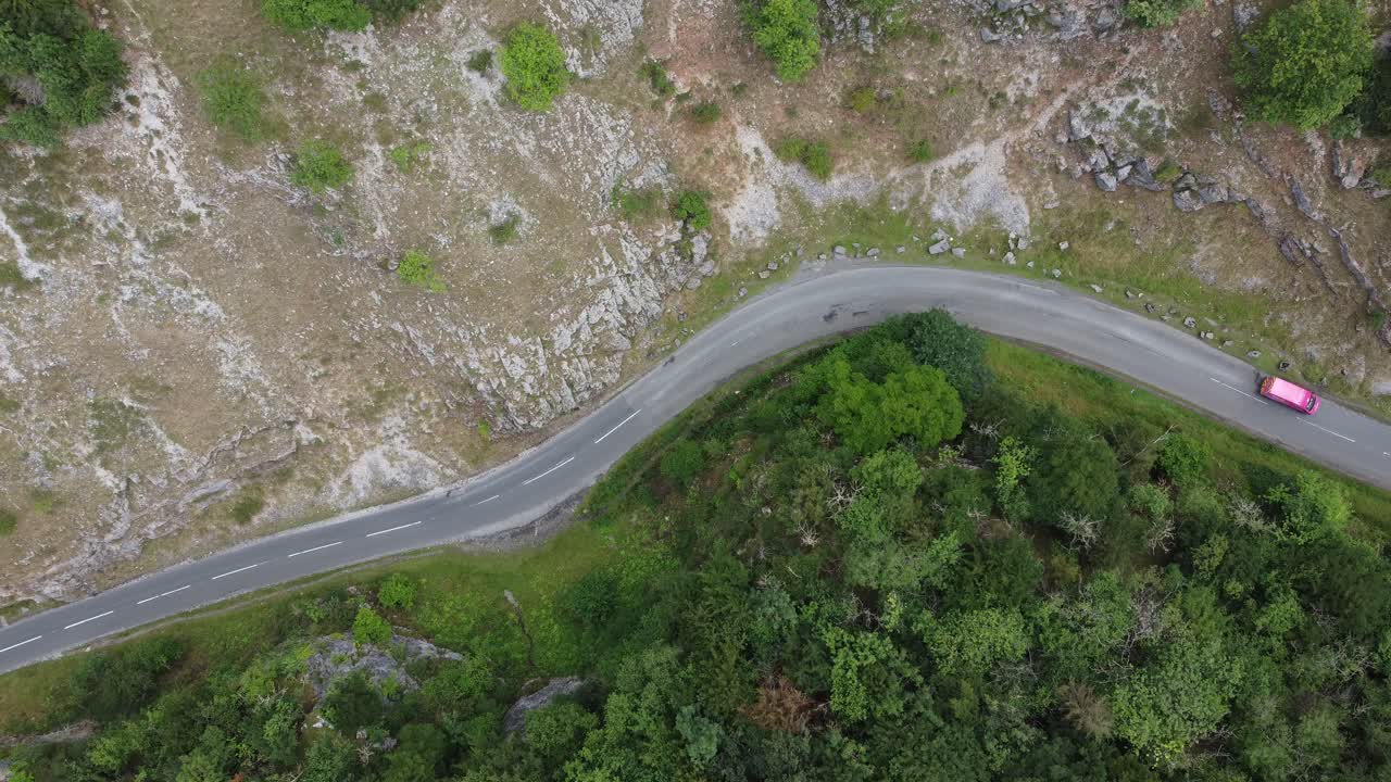 Static top down aerial view of cars driving along a winding road at Cheddar gorge in the Mendip Hills, Somerset, UK with forest on one side and rocky cliffs on the other