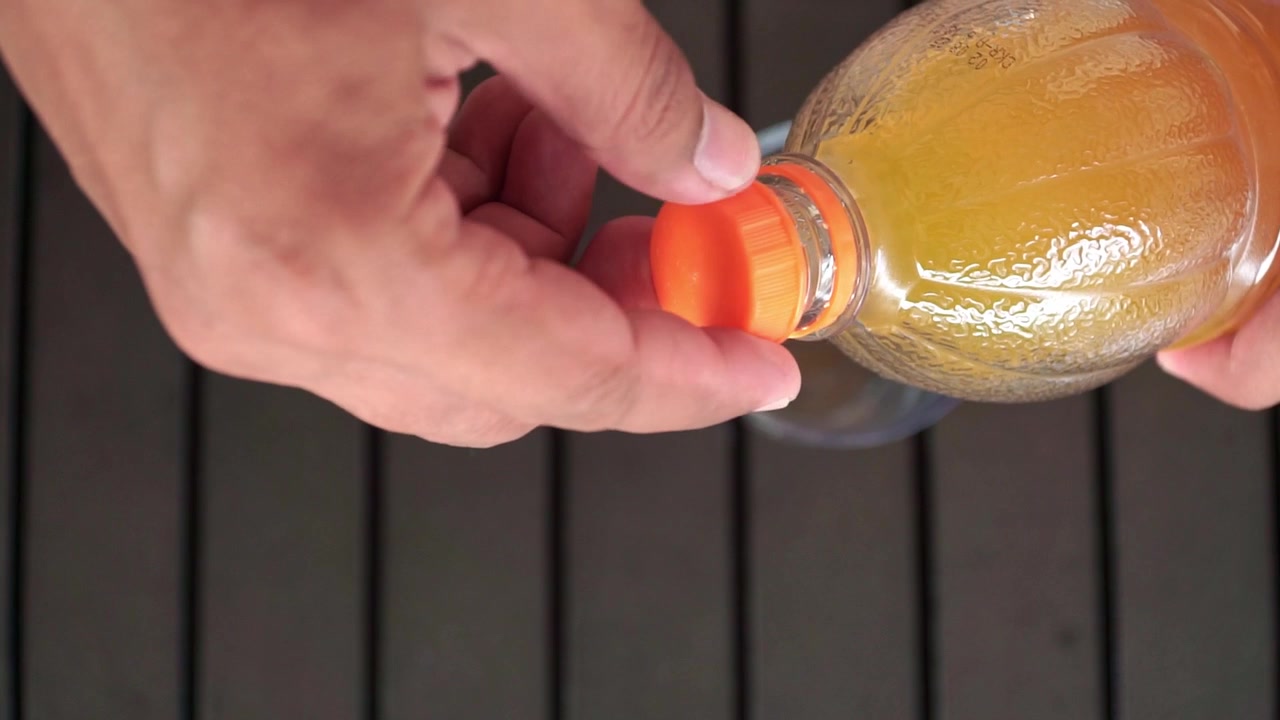 Una mano humana gira la tapa para abrir una botella de zumo de naranja. Perfecto para temas de estilo de vida saludable, desayuno, refresco y bebidas.