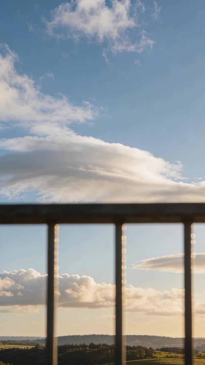 Video vertical: Nube en movimiento desplazándose sobre un valle desde un balcón, el viento empuja la nube más allá de una barandilla de metal.