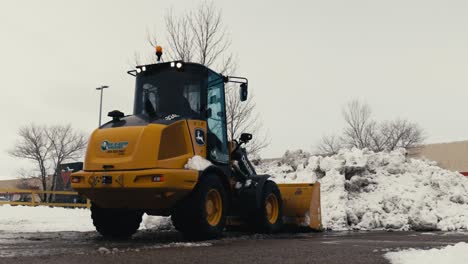 yellow wheel loader clearing snowy lot. winter snowplow