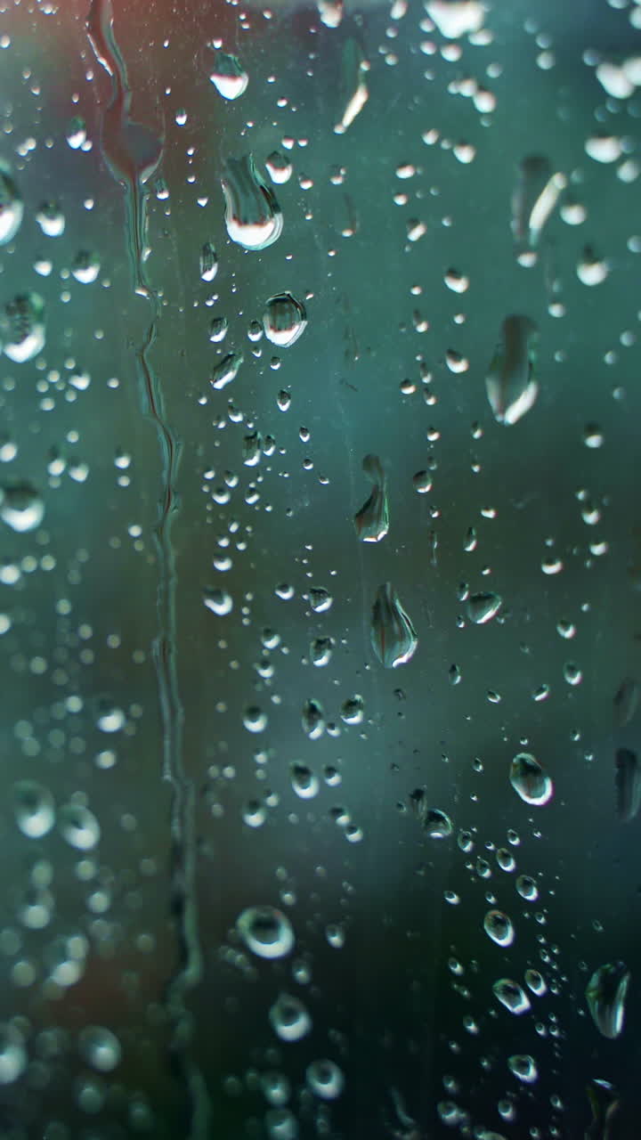 Glass window in rainy weather with raindrops. Falling drops. Wet window with drops and white dots. Close-up. Vertical video