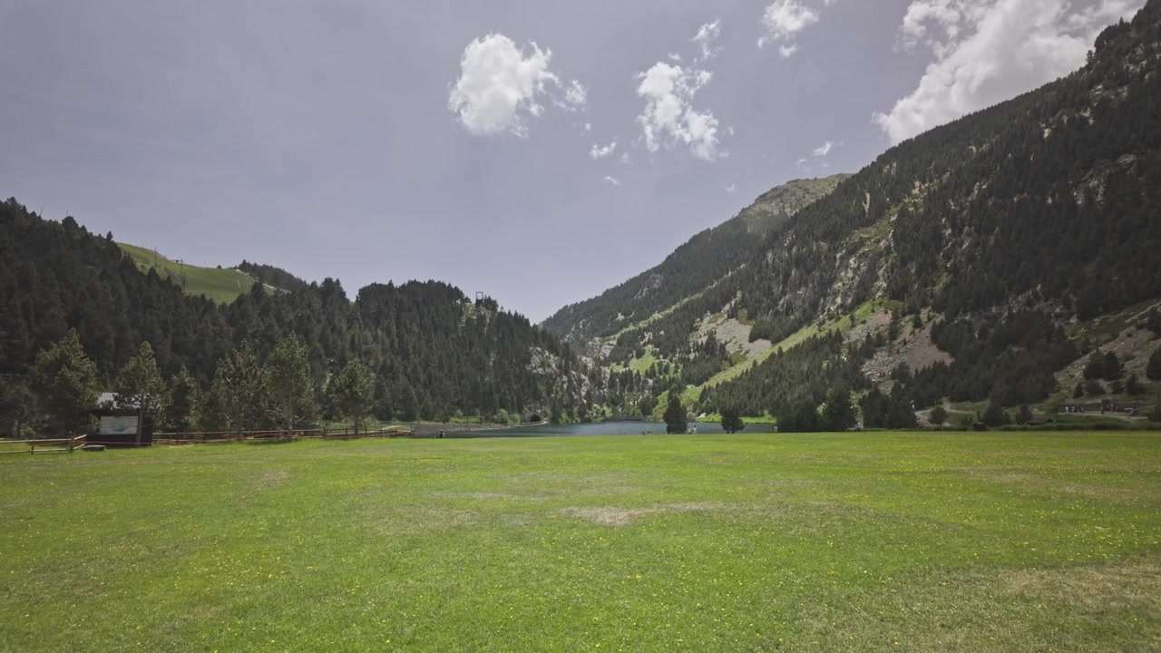 Splendida vista panoramica del paesaggio naturale nella Vall de Nuria, che mostra il prato verde lussureggiante, il bacino idrico e le maestose montagne dei Pirenei sotto un cielo estivo parzialmente nuvoloso.
