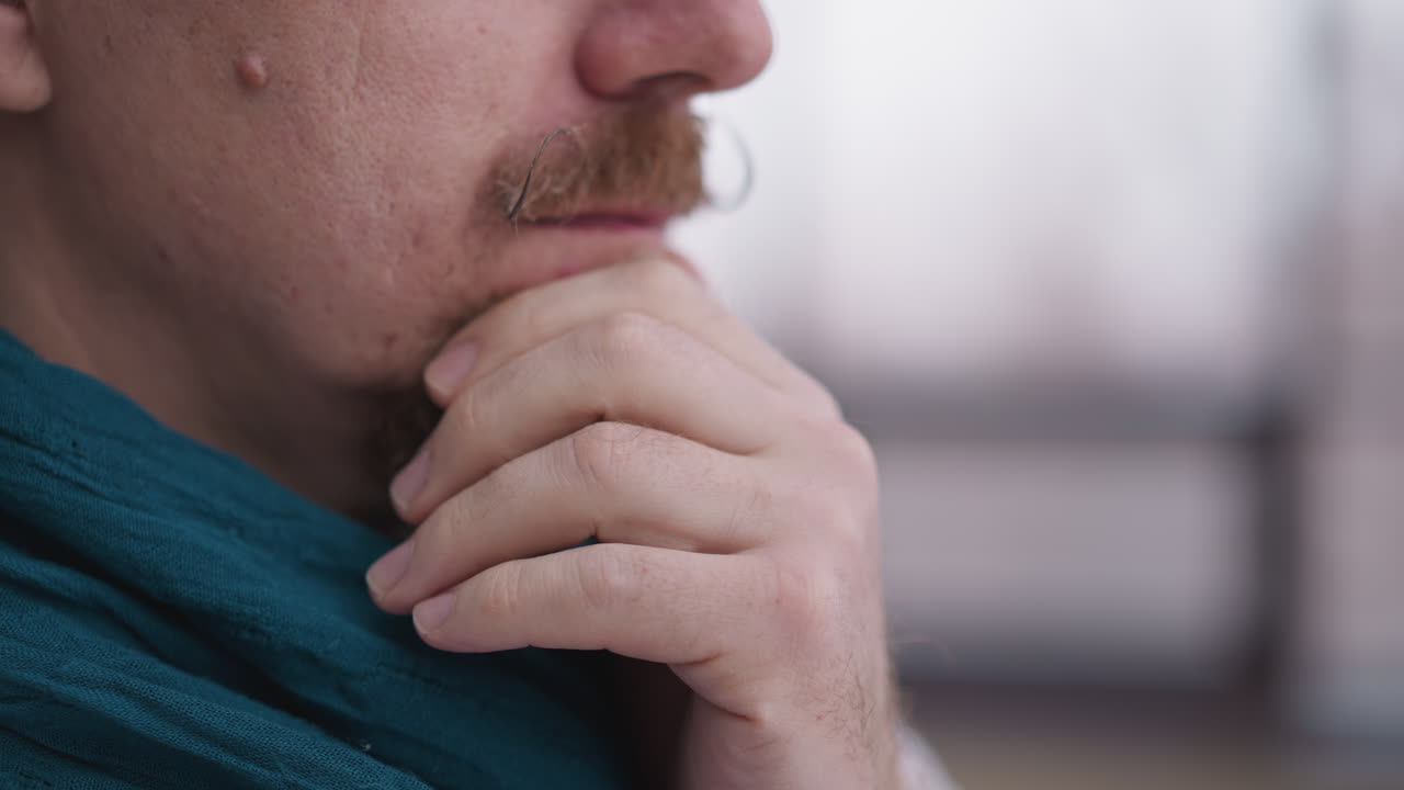hombre con pañuelo coloca la mano en el mentón de cerca. hombre enfocado toma un momento para apreciar el paisaje cubierto de nieve fuera de la ventana en la residencia. tranquilidad disfrute