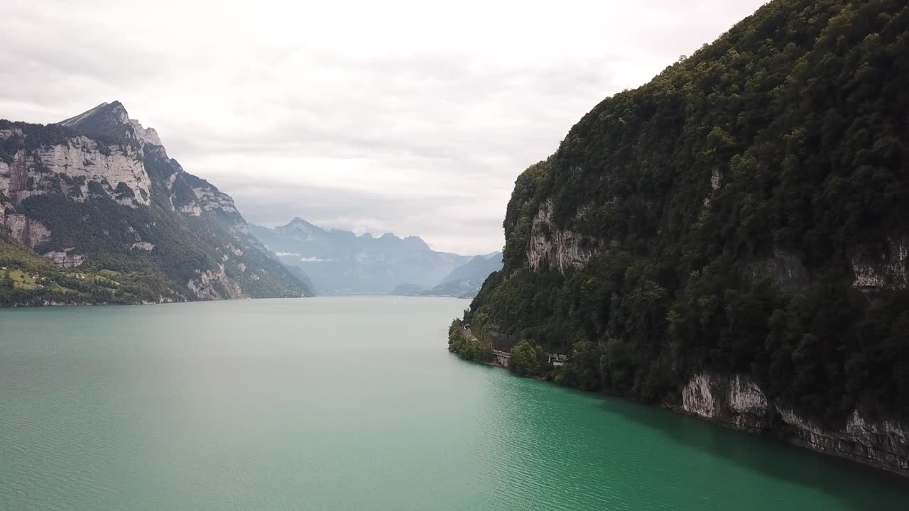Amazing rural turquoise colored lake Walensee between Switzerland mountains of the alps where trees are growing. Drone dolly shot on a cloudy day