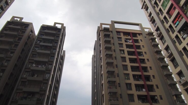 Vista de baixo de complexos residenciais multifamiliares contemporâneos em cidade indiana, com design arquitetônico moderno sob céu nublado.