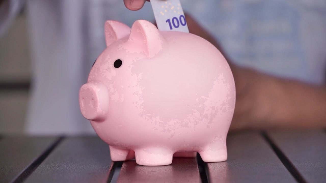 Hand of person depositing money into pink piggy bank, money management and financial growth concept.
