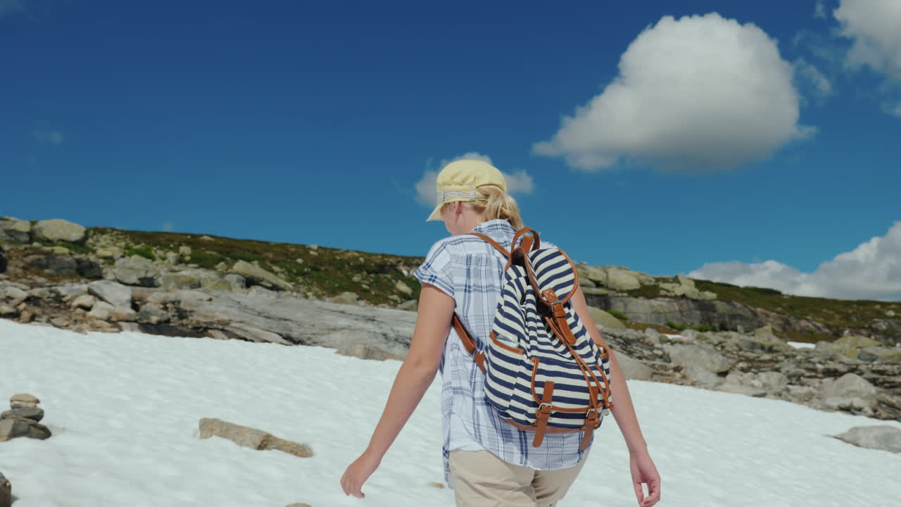 한 여자가 밖에 산에서 눈 위를 걷고 있습니다. 더운 여름입니다. 눈이 녹지 않았습니다.