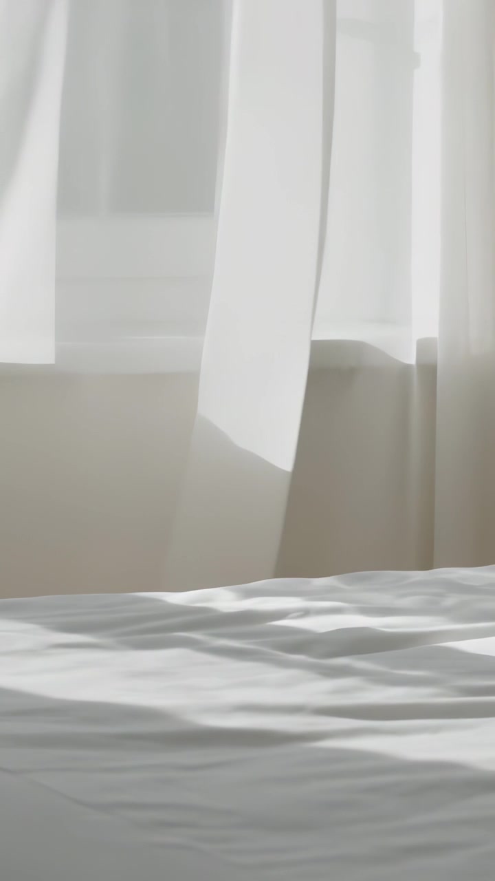 Video vertikal: Angin pagi mengibarkan tirai tipis di jendela kamar tidur, menyinari tempat tidur.