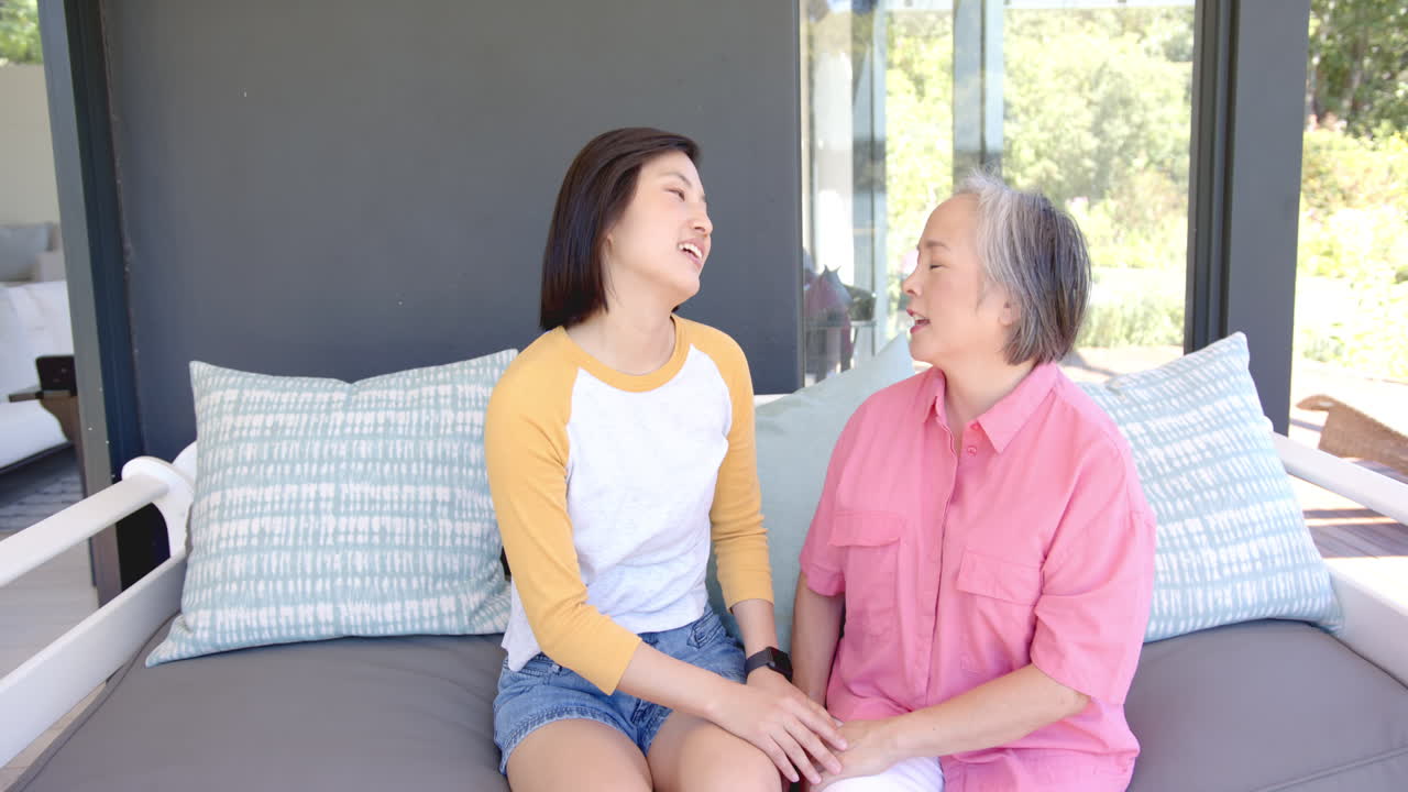Laughing together, elderly asian woman and young asian woman sitting on couch at home
