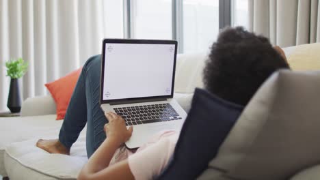 happy african american woman sitting on sofa, using laptop with copy space