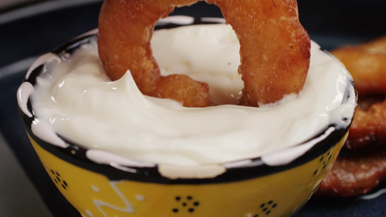Fried crispy onion rings dipping in white creamy sauce close-up macro. Roasted onion rings for snacks at bar, cafe. Fast food. Delivery. Beer snacks