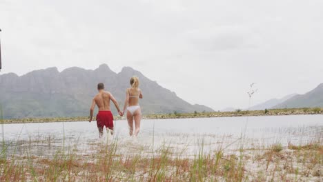 Caucasian-couple-having-a-good-time-on-a-trip-to-the-mountains,-wearing-bathing-suits-and-running-in