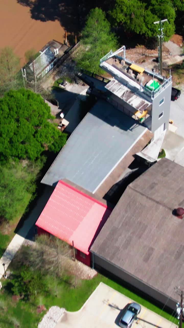 Vertical drone footage of the Tensas Tower on the Teche in New Iberia, Louisiana. The scene shows the contemporary riverfront lodging, off-street parking, boat docking, and marina on the Bayou Teche