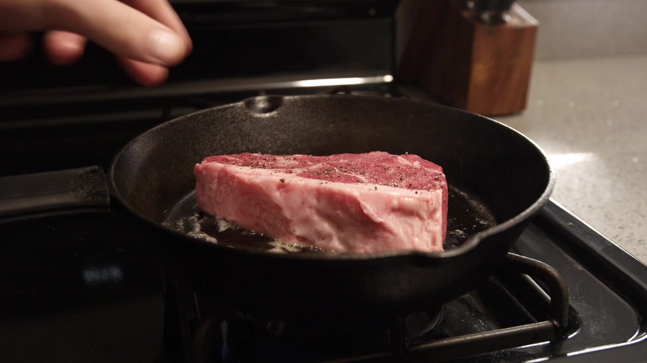 Mettere una bistecca fresca in una padella di ghisa sfrigolante riempita con burro, olio e aglio. Cuocere la carne di manzo.