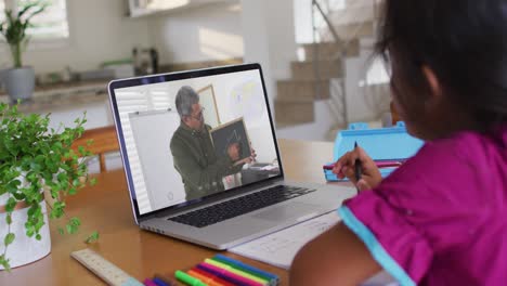 African-american-girl-doing-homework-while-having-a-video-call-with-male-teacher-on-laptop-at-home