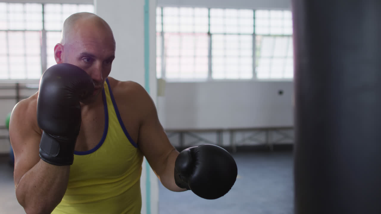 entrenador masculino caucásico con guantes de boxeo entrenando con saco de boxear en el gimnasio