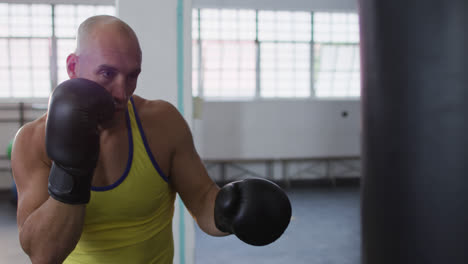 Caucasian-male-trainer-wearing-boxing-gloves-training-with-punching-bag-at-the-gym