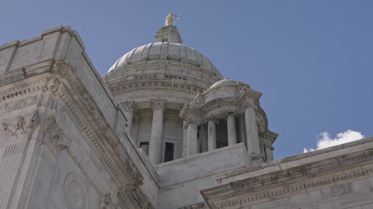 Ampia ripresa cinematografica con movimento verticale verso l'alto da un lampione decorativo alla cupola di marmo della Rhode Island State House a Providence in una luminosa giornata estiva.