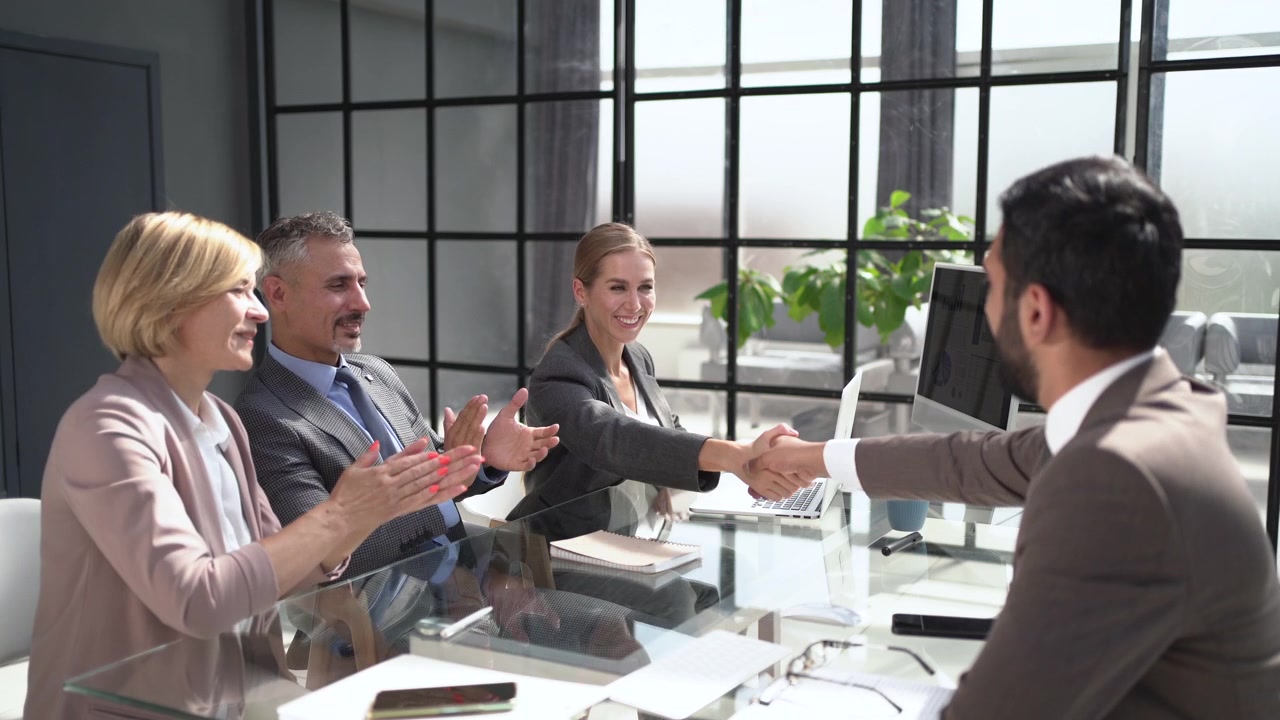 Businesswoman Shakes Hands with Colleague as Team Claps in Office