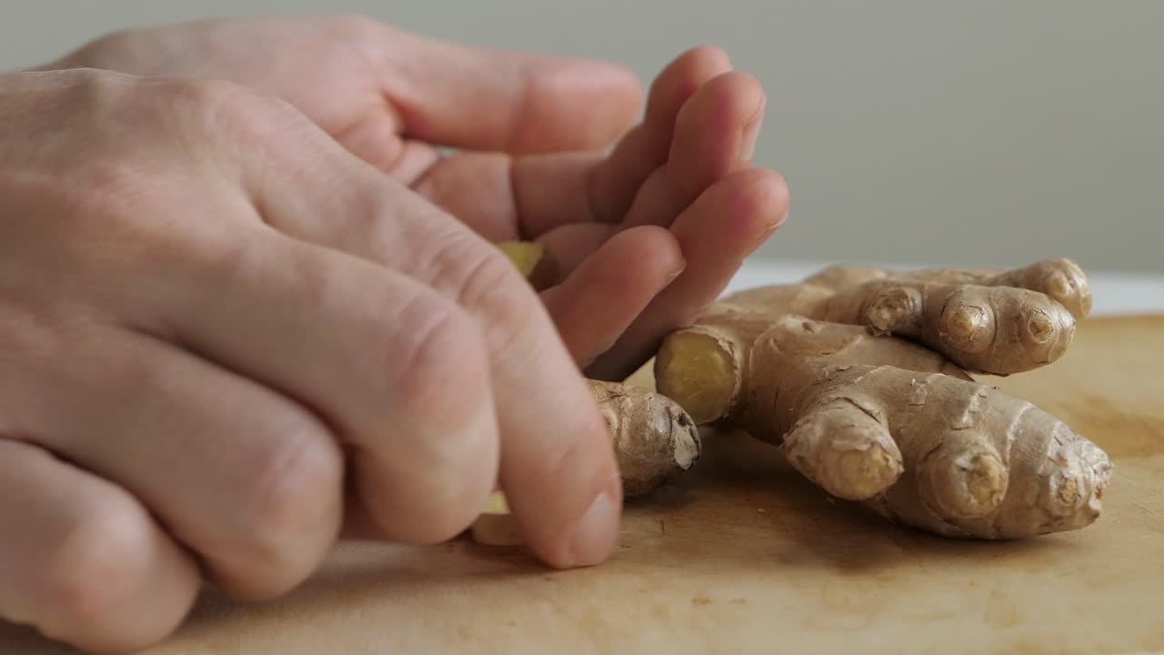 hombre recogiendo raíz de jengibre en rodajas en la tabla de cortar, comida saludable, de cerca