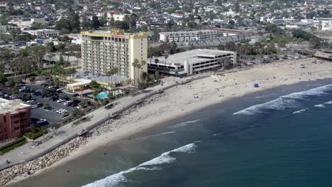 Ventura-Beach,-California-as-the-surf-rolls-in-on-the-sand-with-hotels,-restaurants-and-popular-tourist-destinations---aerial-flyover