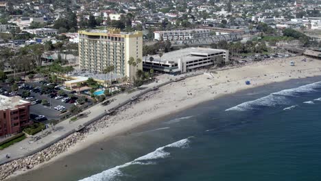 ventura beach, california as the surf rolls in on the sand with hotels, restaurants and popular tourist destinations - aerial flyover