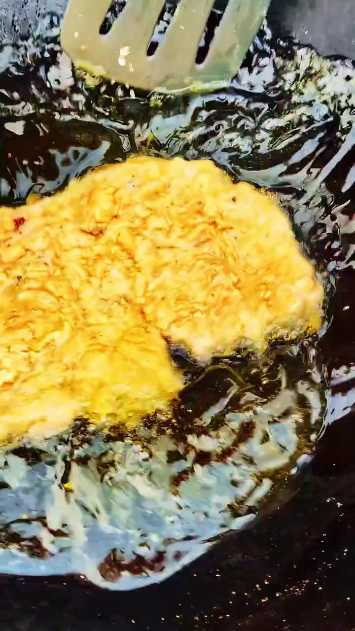 A golden omelette sizzles in hot oil, with red tongs and a spatula adjusting it. Ideal for cooking tutorials or culinary blogs.