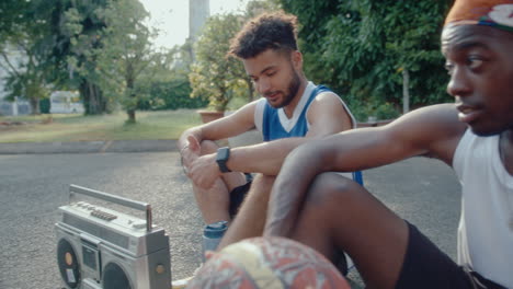 friends sitting with boombox and talking on outdoor basketball playground