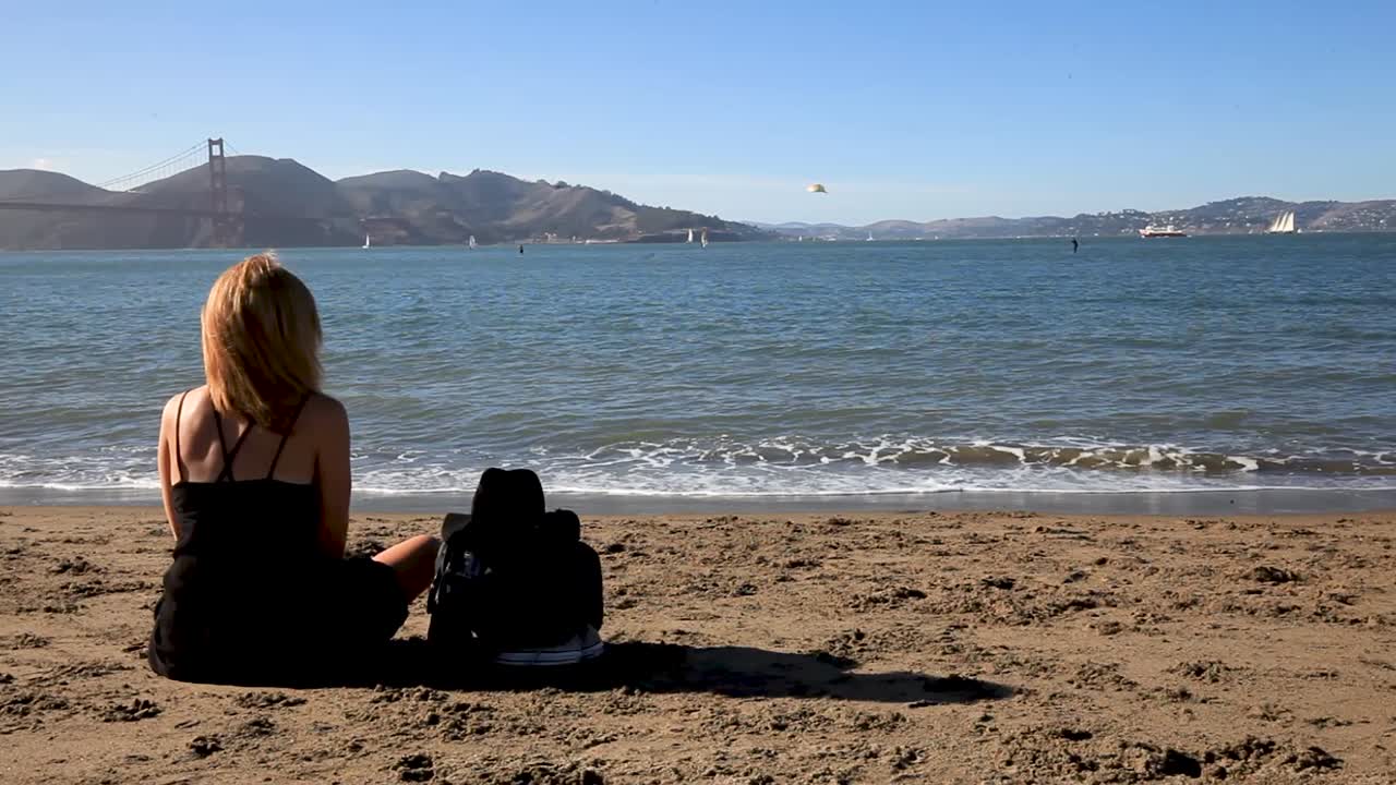 그녀는 금문교를 응시하면서 해안에서 휴식을 취하는 여성