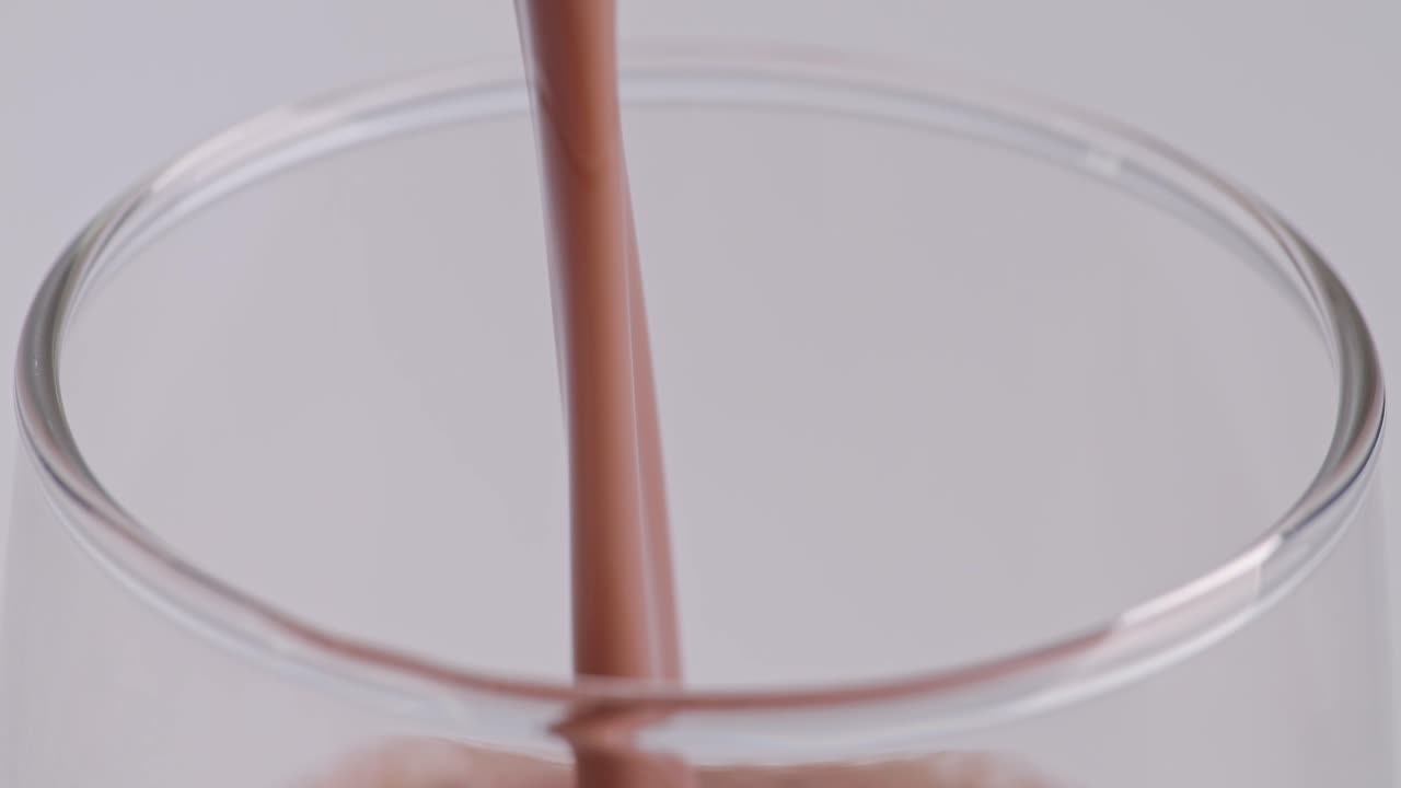 Primo piano di bevanda al latte al cioccolato versata al rallentatore in un bicchiere tumbler su sfondo bianco