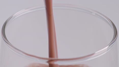 close up of slow motion pour chocolate milk drink in tumbler glass on white background