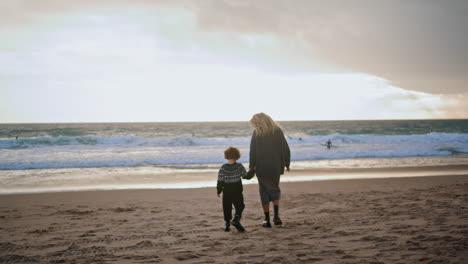 mother son walking beach holding hands rear view. carefree family resting sunset