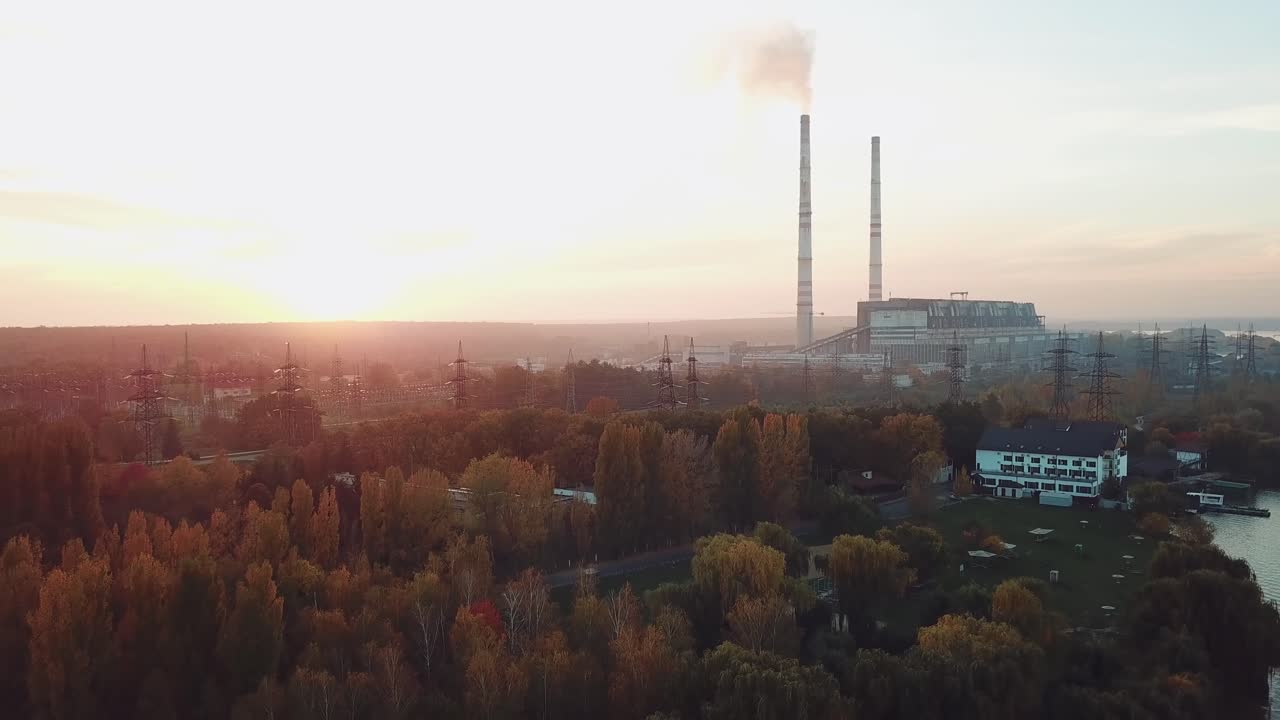 power plant with two pipes is located on the outskirts of the city on the bank of river. Camera motion back. Aerial view