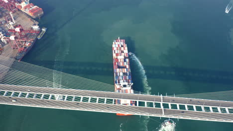 buque portacontenedores rojo asistido por remolcadores de remolque y empuje que navegan hacia el muelle en una terminal de contenedores mientras pasan el puente de los canteros
