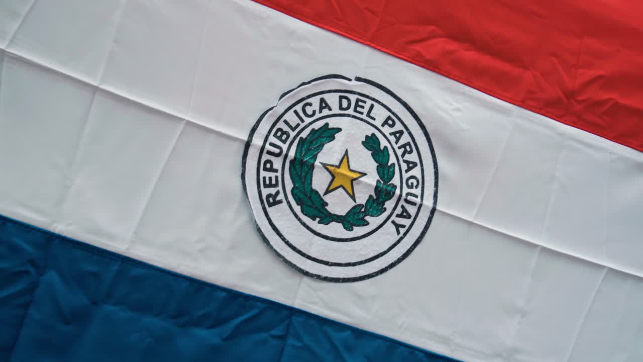 A detailed close-up of the national emblem of Paraguay displayed on a flag. The emblem represents the country's identity, history, and cultural heritage in detail