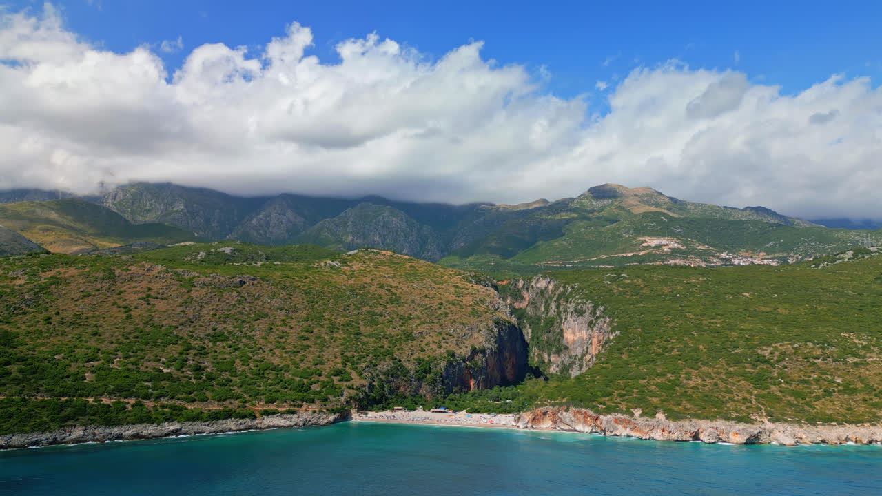 Aerial drone shot flying high in distance over Gjipe beach, Albania with mountain range in the background on a sunny day