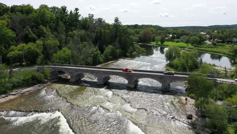 Der-Rote-Vintage-LKW-überquert-Die-Steinbrücke-Und-Den-Malerischen-Bach-Im-Land