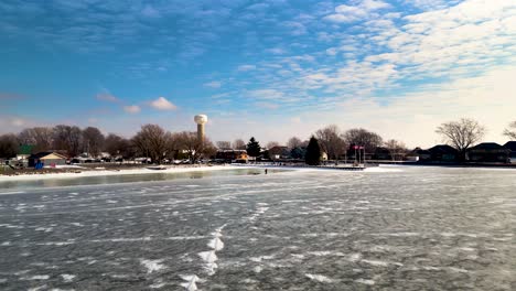 Man-walking-on-frozen-lake-with-ice-sled-St-Clair,-Mitchell's-Bay-in-the-background,-with-blue-sky-in-winter-60fps-aerial-drone-shot