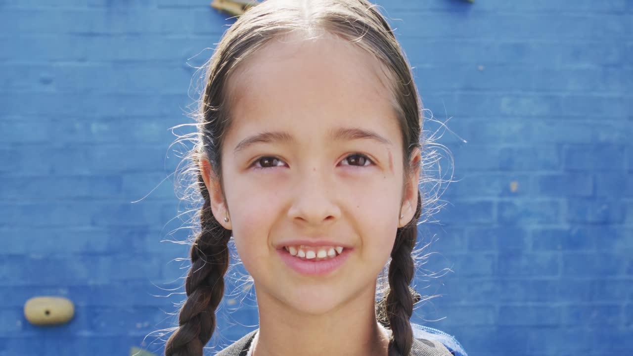 retrato de una estudiante biracial feliz mirando a la cámara con una pared de escalada en el fondo