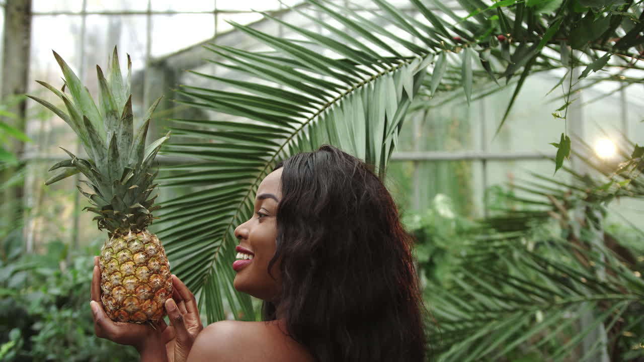 Jeune et belle fille de profil tenant un ananas dans ses mains et souriant à la caméra